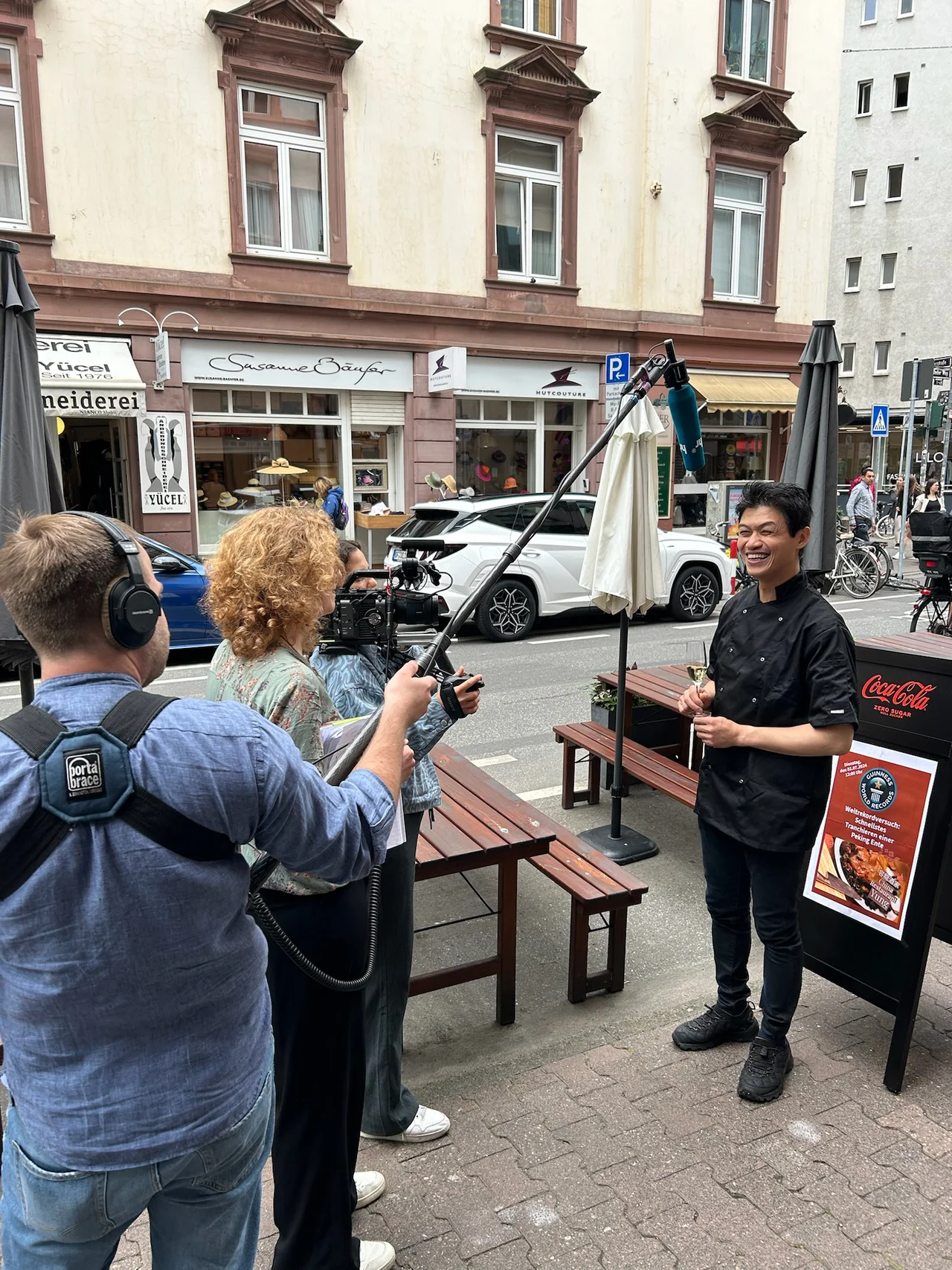 Chi Kei Yung lächelt vor dem China Restaurant Yung in Frankfurt, Reporter mit Boom-Mic interviewt ihn