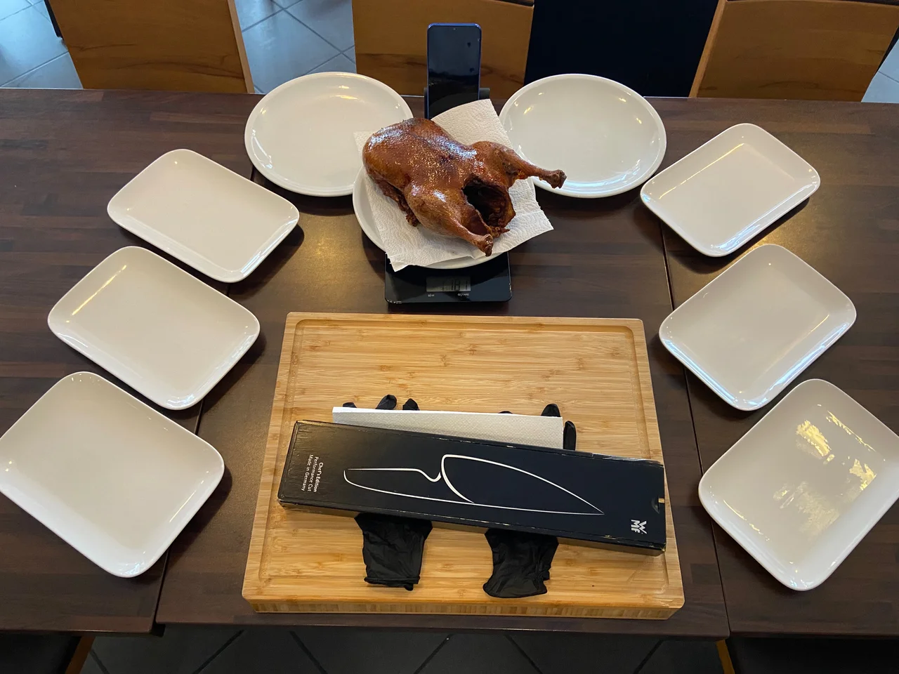 Trainings-Setup mit ganzer Pekingente auf Küchenwaage, sechs Tellern im Kreis und WMF-Messer